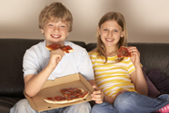 a teenage boy and girl watching television and eating pizza