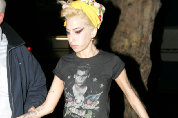Amy Winehouse with blonde hair is lead down the street by a man_rex