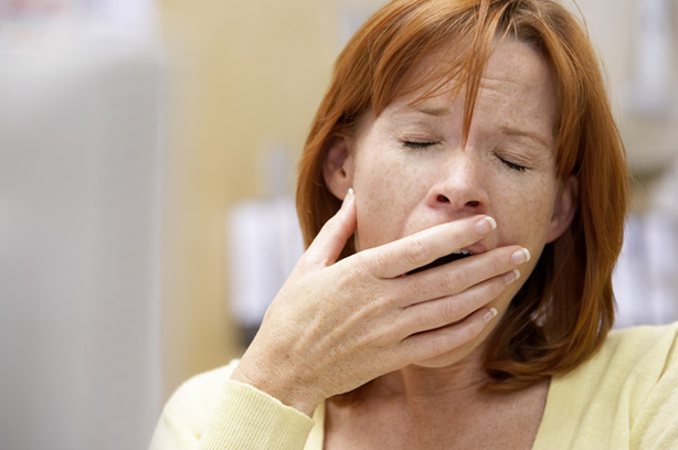 Woman with red hair and green jumper yawning